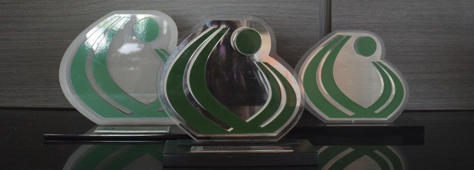 Tres trofeos transparentes con un diseño verde en forma de espiral sobre un fondo oscuro.