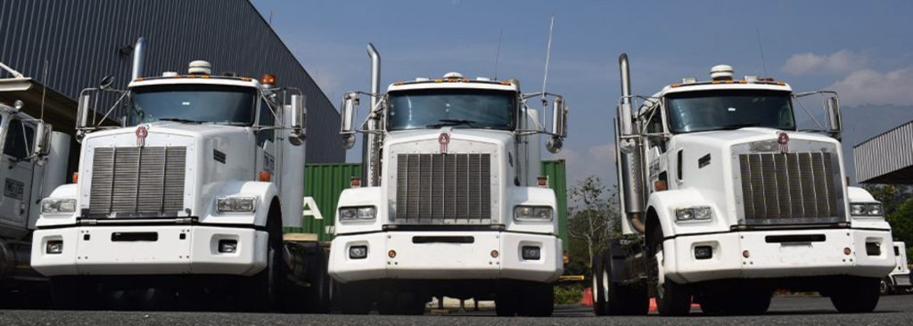 Tres camiones de carga blancos estacionados en línea frente a un edificio industrial, bajo un cielo despejado.