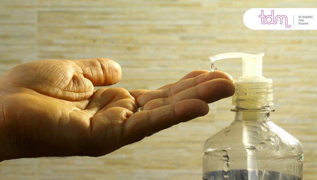 Mano presionando un dispensador de jabón líquido con el logotipo de "tdm" en la esquina superior derecha.