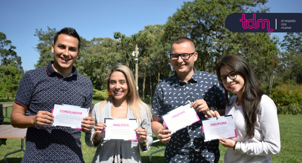 Cuatro personas sonrientes sostienen tarjetas con palabras: "Conciliador", "Analítico", "Creativo" y "Disciplina". Están al aire libre.
