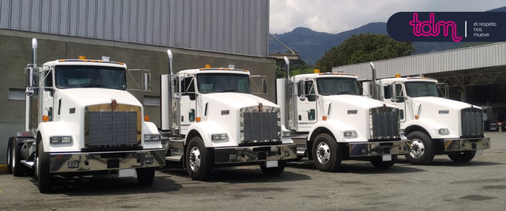 Cuatro camiones blancos estacionados en fila frente a un edificio industrial.
