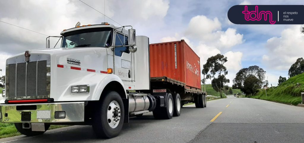 Camión blanco con contenedor rojo en una carretera vacía; logo de "tdm" en la esquina superior derecha.