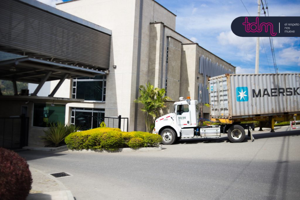 Un camión de carga con un contenedor de Maersk se dirige hacia un edificio industrial moderno.