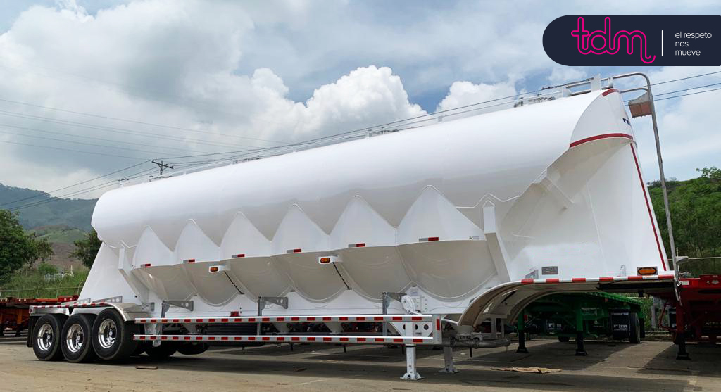 Remolque cisterna blanco estacionado al aire libre con montañas y cielo nublado de fondo; logotipo de empresa en la esquina.