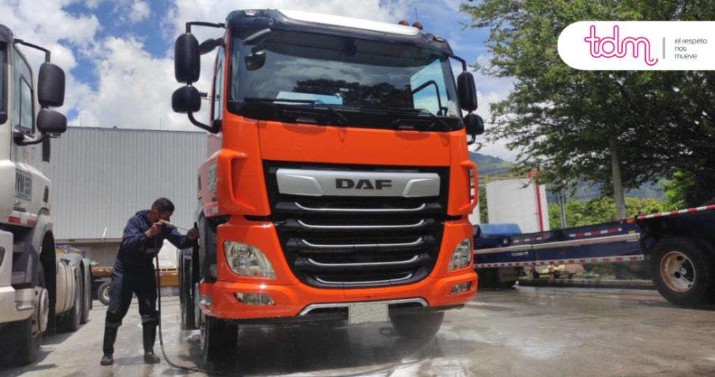 Camión DAF naranja siendo lavado por una persona con una manguera en un área exterior.