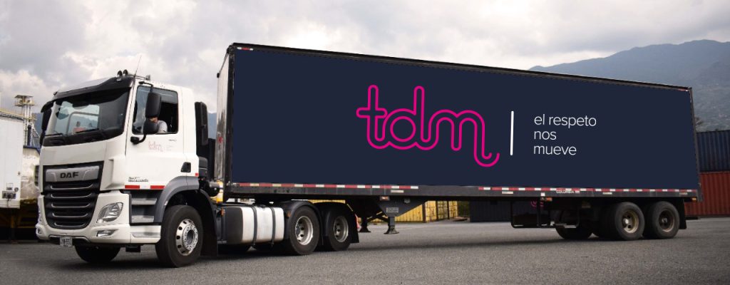 Camión de carga con remolque negro, logo "tdm" y texto "el respeto nos mueve" estacionado en un área industrial.
