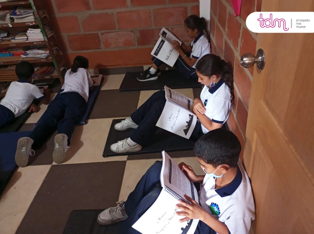 Estudiantes leen libros sentados y recostados en una sala con paredes de ladrillo.