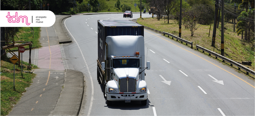 Camión blanco circulando por una carretera con señal de "Pare" a la izquierda y un coche en el fondo.