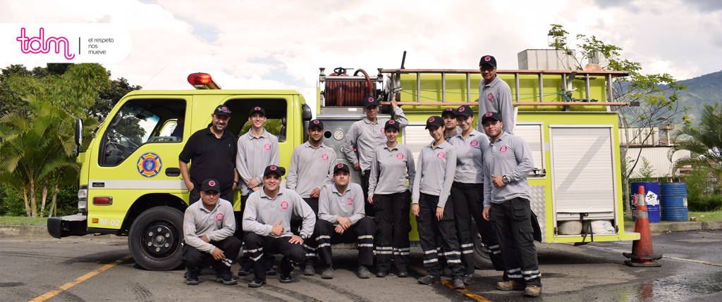 Un grupo de bomberos sonríe frente a un camión de bomberos amarillo con equipo y escaleras.