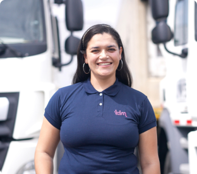 Mujer sonriente con camiseta azul de pie frente a camiones blancos.