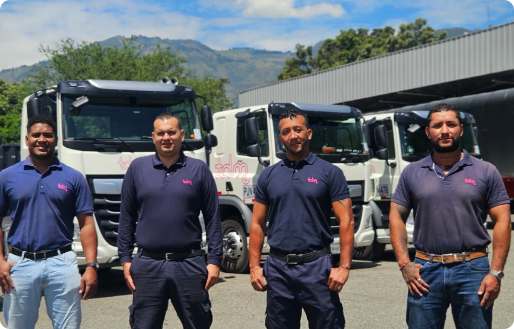 Cuatro hombres con camisetas de trabajo azul posan frente a varios camiones estacionados.