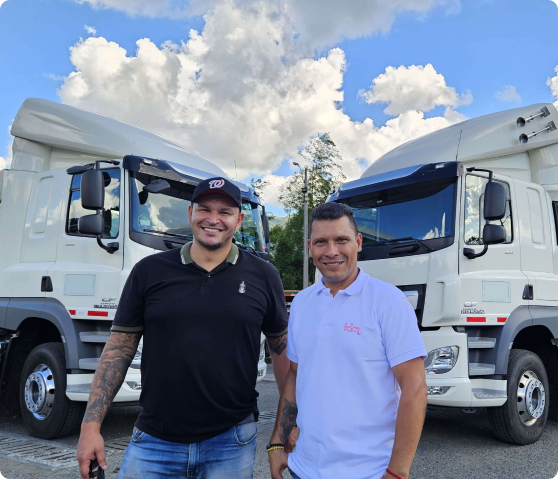 Dos hombres sonrientes posan frente a dos camiones blancos al aire libre.