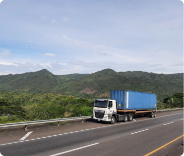 Camión con un contenedor azul estacionado en una carretera frente a un paisaje montañoso y vegetación.