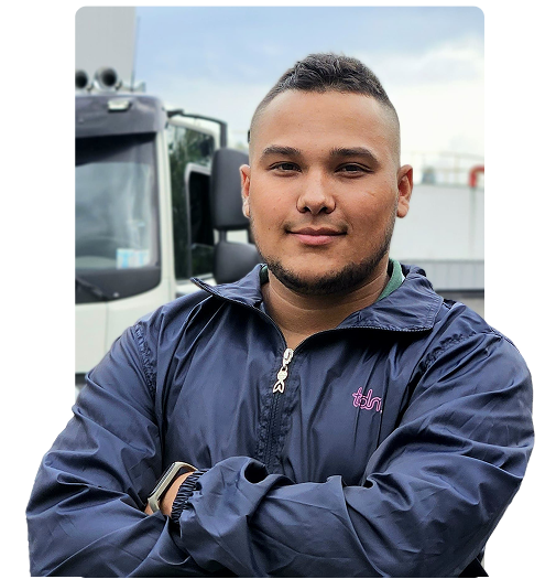 Persona con chaqueta azul, de pie con los brazos cruzados frente a un camión.