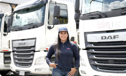 Una persona vestida con uniforme azul y gorra está de pie frente a varios camiones blancos con el logotipo "tdm" visible.